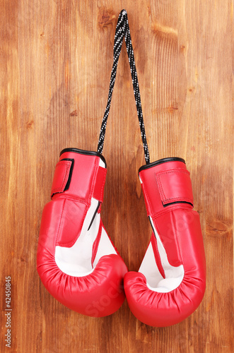 Red boxing gloves hanging on wooden background © Africa Studio