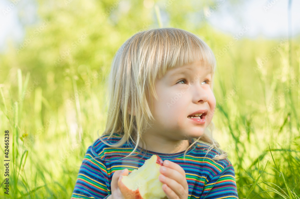 Adorable baby eat red apple sitting on grass in park Adorable baby eat red apple sitting on grass in park