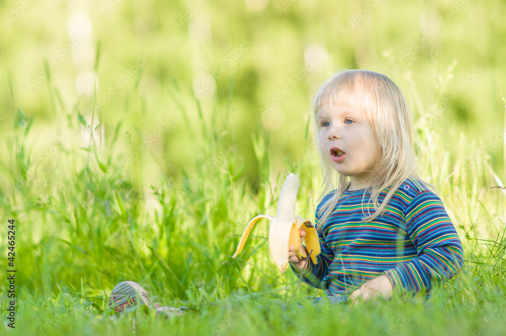Adorable baby eat banana sitting on grass in park Adorable baby eat banana sitting on grass in park