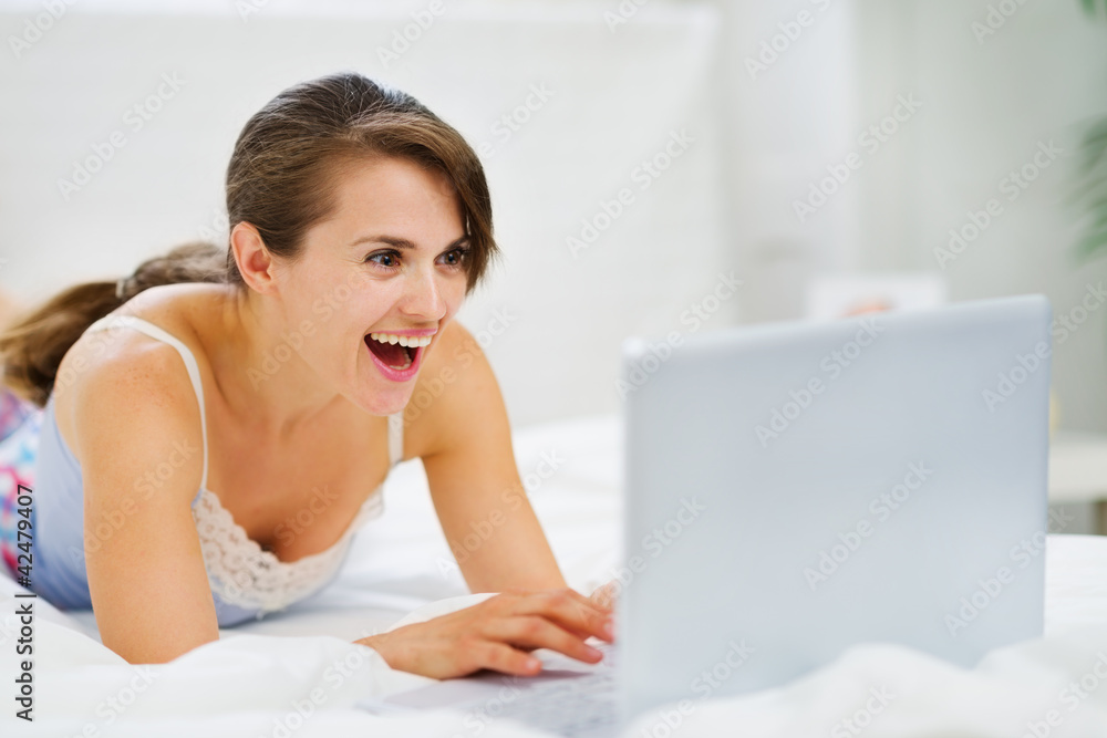 Woman laying on bed and suprisely looking in laptop Woman laying on bed and suprisely looking in laptop