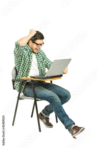 A shocked student sitting on a chair and working on a laptop