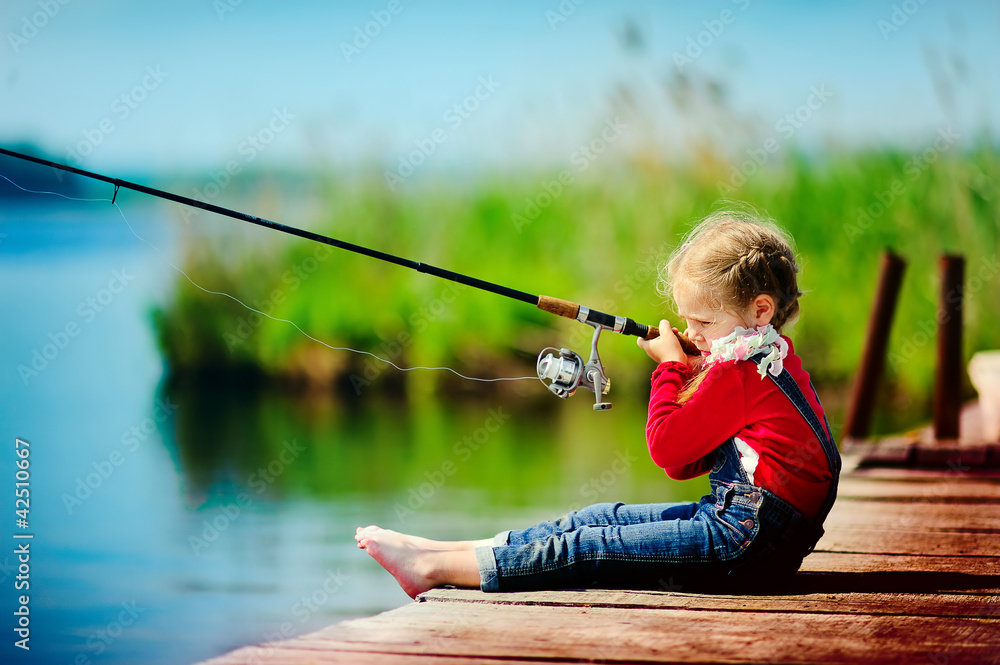 little girl fishing from wooden dock on lake little girl fishing from wooden dock on lake