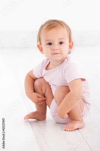 Cute baby girl crouching on floor photo