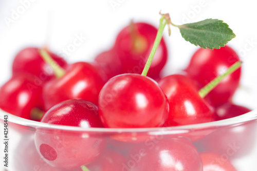 cherry with green leaf and a cup of cherries on a white backgrou