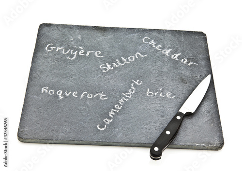 Slate cheese board with cheede names and knife on white backgrou