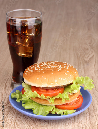 Big and tasty hamburger on plate with cola on wooden table