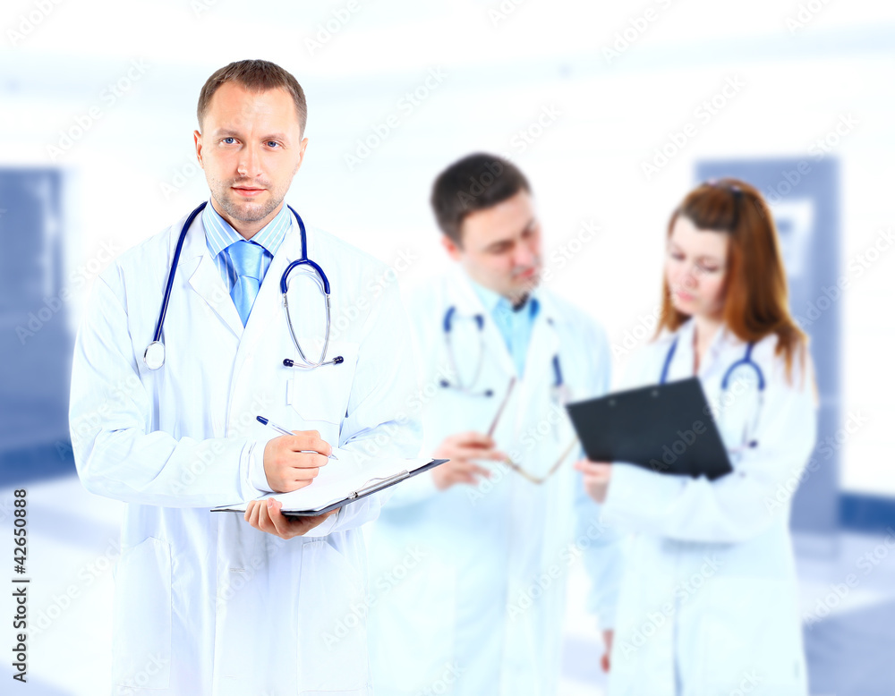 Portrait doctor smiling with colleagues in background Portrait doctor smiling with colleagues in background