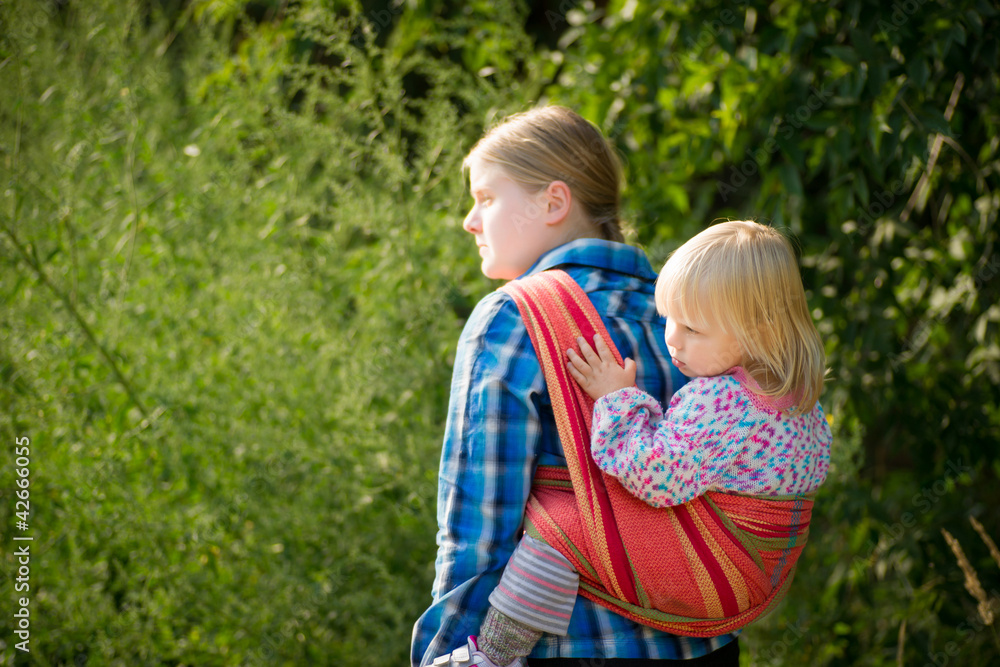 Mother with daughter in sling on back Mother with daughter in sling on back
