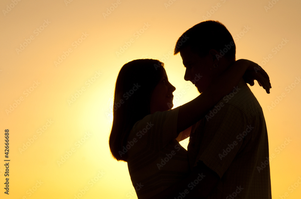 Silhouettes of young couple hugging on sunny summer day