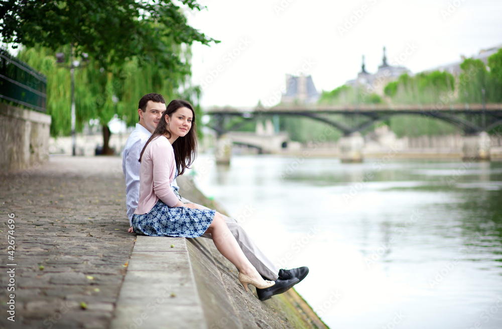 Joyful couple is sitting on the embankment in Paris