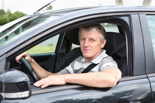 Mature male sitting in black car on driver seat