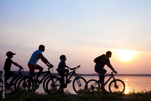 family on bicycles admiring the sunset on the lake. silhouette
