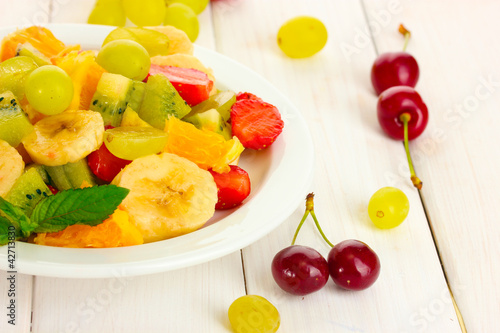 Fresh fruits salad on plate and berries on white wooden table