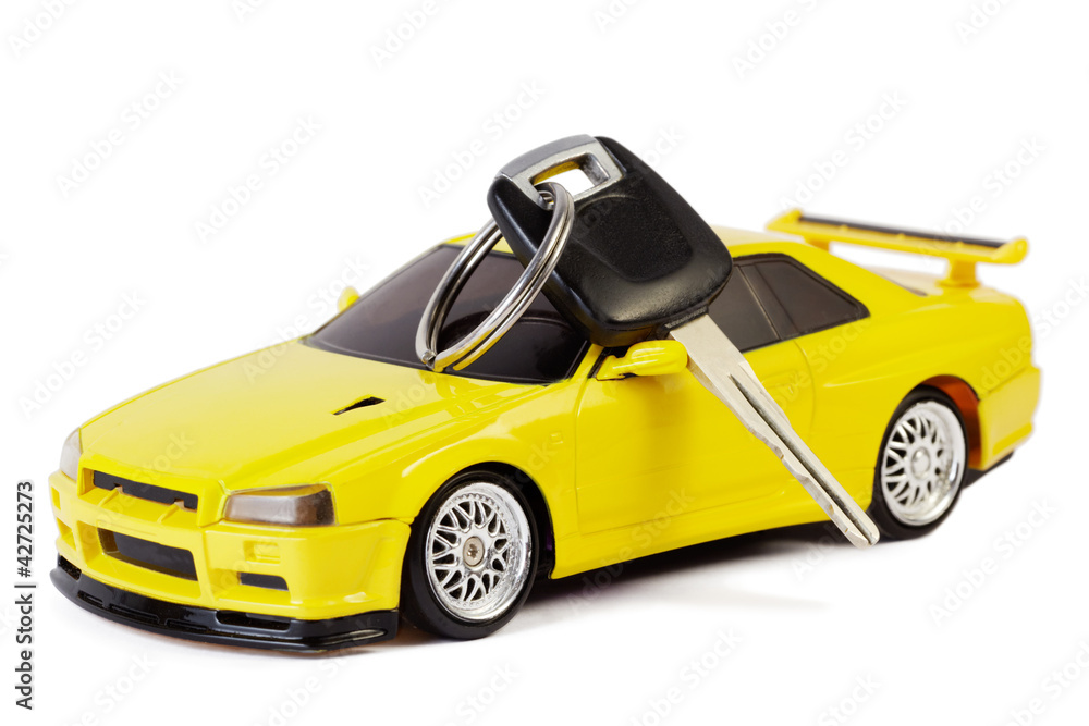 Fototapeta premium Car key lays on the yellow toy car, isolated on white