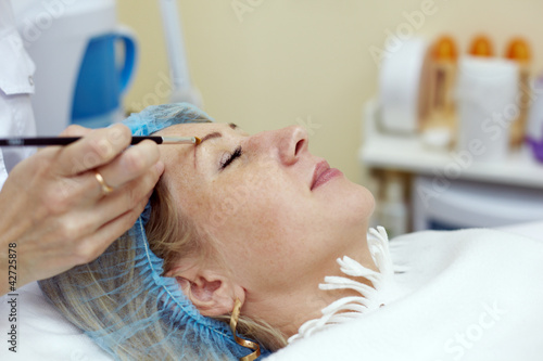 Hands of beautician that works with eyebrow of woman in salon