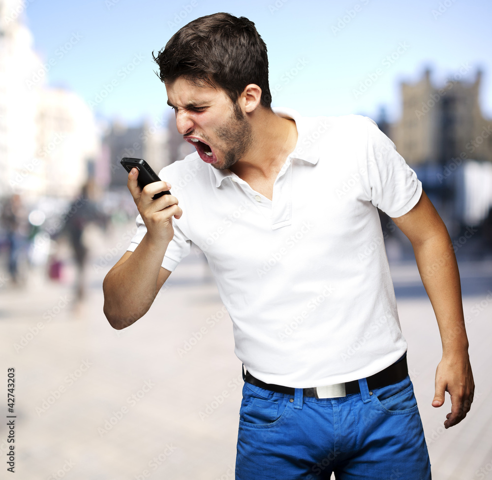 portrait of angry young man shouting using mobile at a crowded s portrait of angry young man shouting using mobile at a crowded s