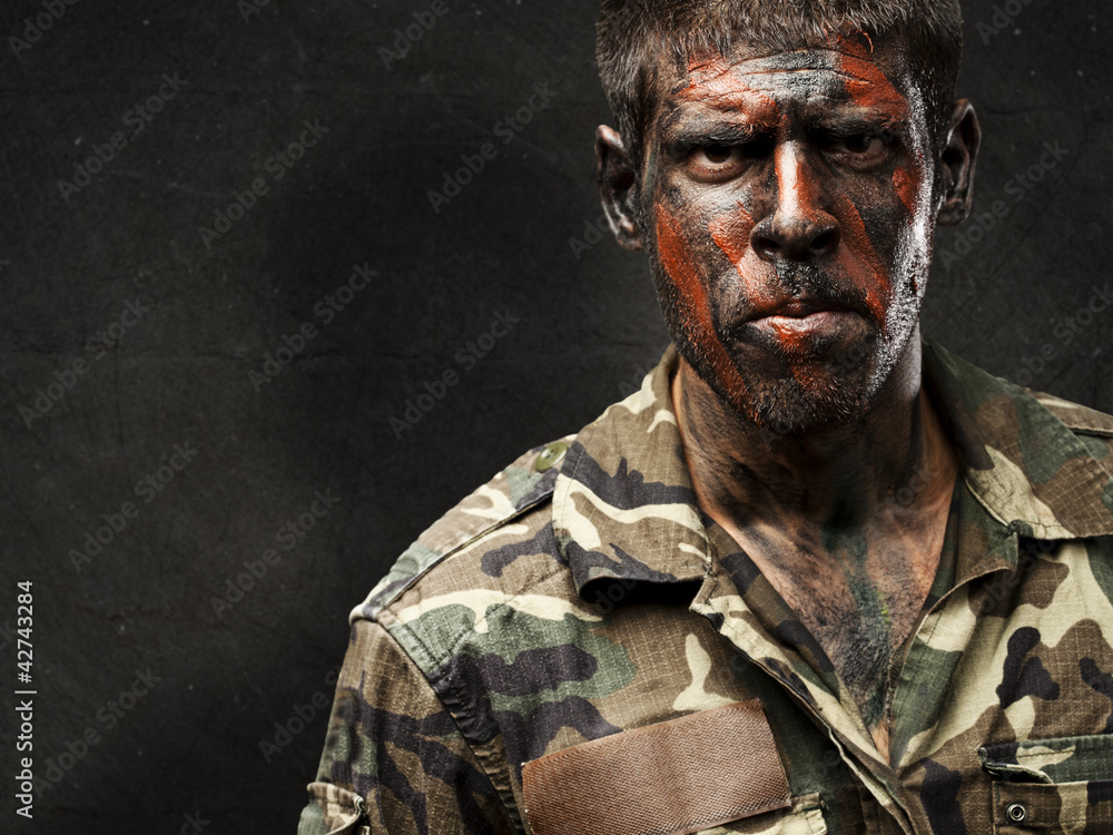 young soldier with camouflage paint looking very serious against young soldier with camouflage paint looking very serious against