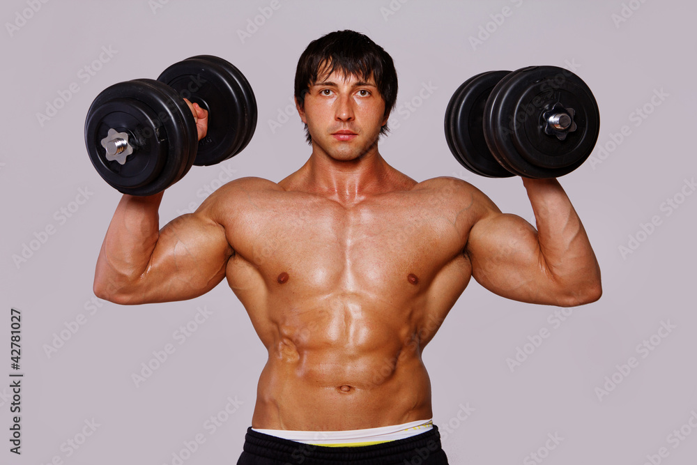 Portrait of muscle man on grey background with dumbbels Portrait of muscle man on grey background with dumbbels