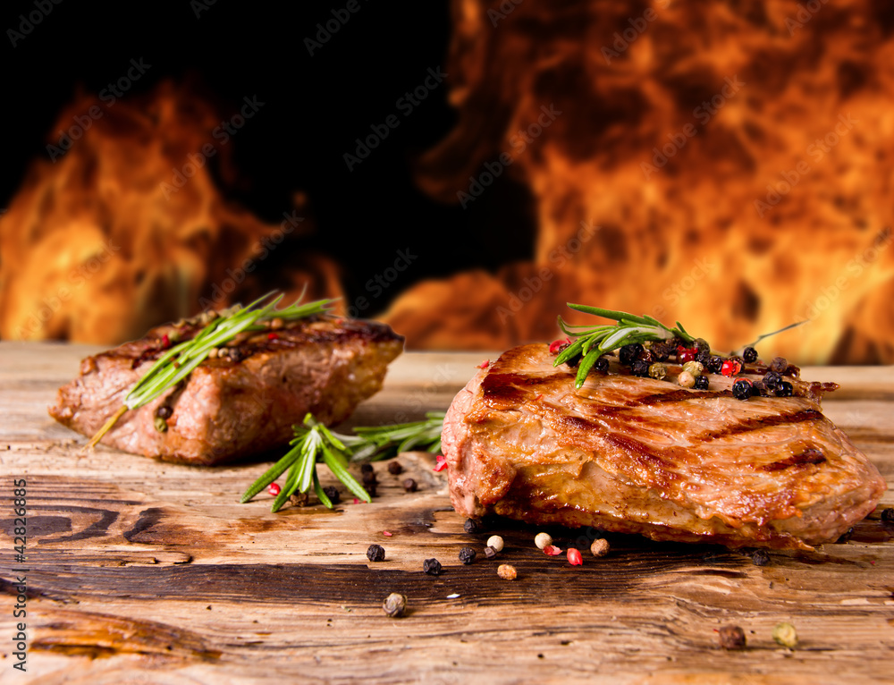 Grilled beef steaks with flames on background
