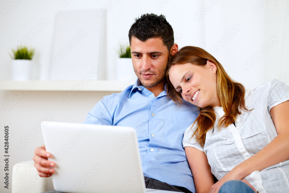 Lovely couple smiling and reading on laptop Lovely couple smiling and reading on laptop