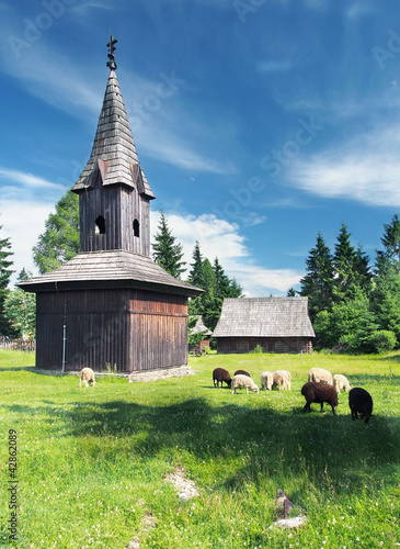 Wooden bell tower with sheep nearby in Pribylina open-air museum