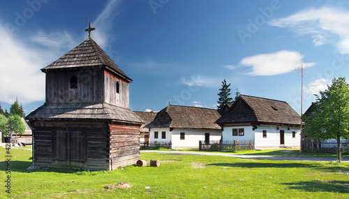 Rare wooden bell tower with folk houses in background.
