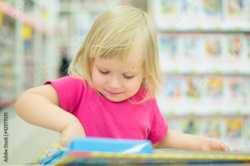 Adorable girl with interactive book on cart in supermarket