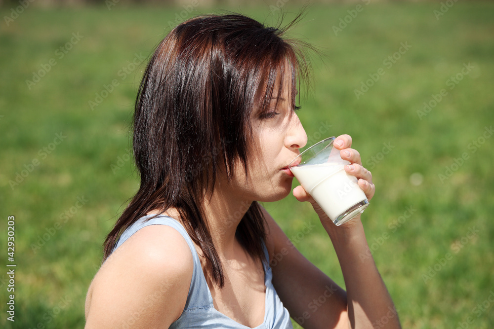 Pretty girl on meadow is drinking glass of milk. Pretty girl on meadow is drinking glass of milk.