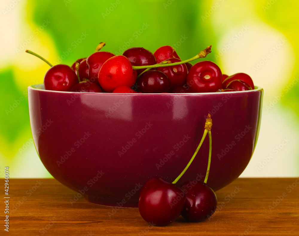 cherry in violet bowl on wooden table on green background cherry in violet bowl on wooden table on green background