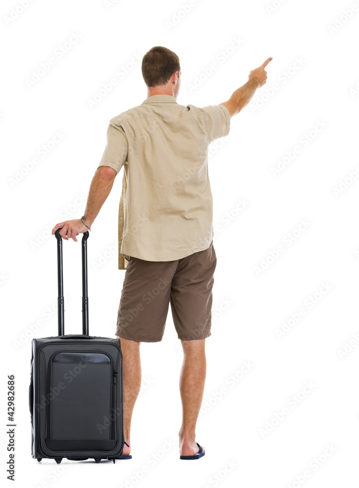 Tourist with wheels bag pointing on copy space. Rear view Tourist with wheels bag pointing on copy space. Rear view