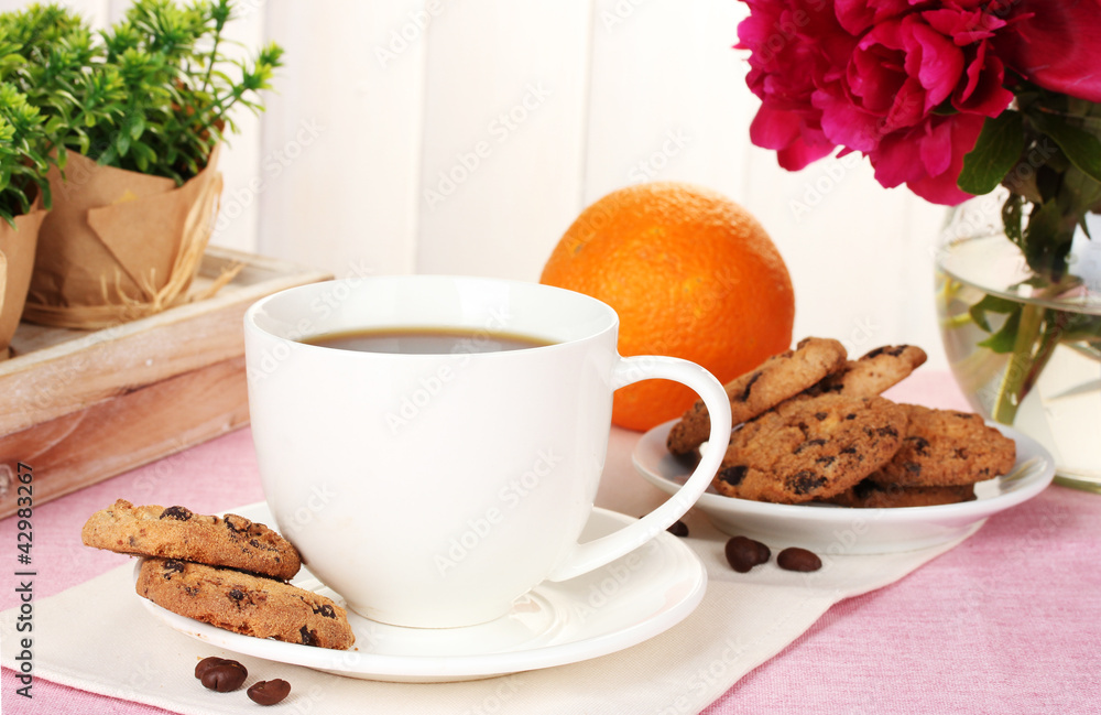 cup of coffee, cookies, orange and flowers on table in cafe