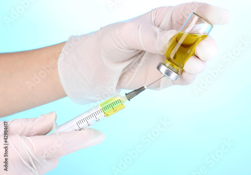 Syringe and medical ampoule in hands on blue background