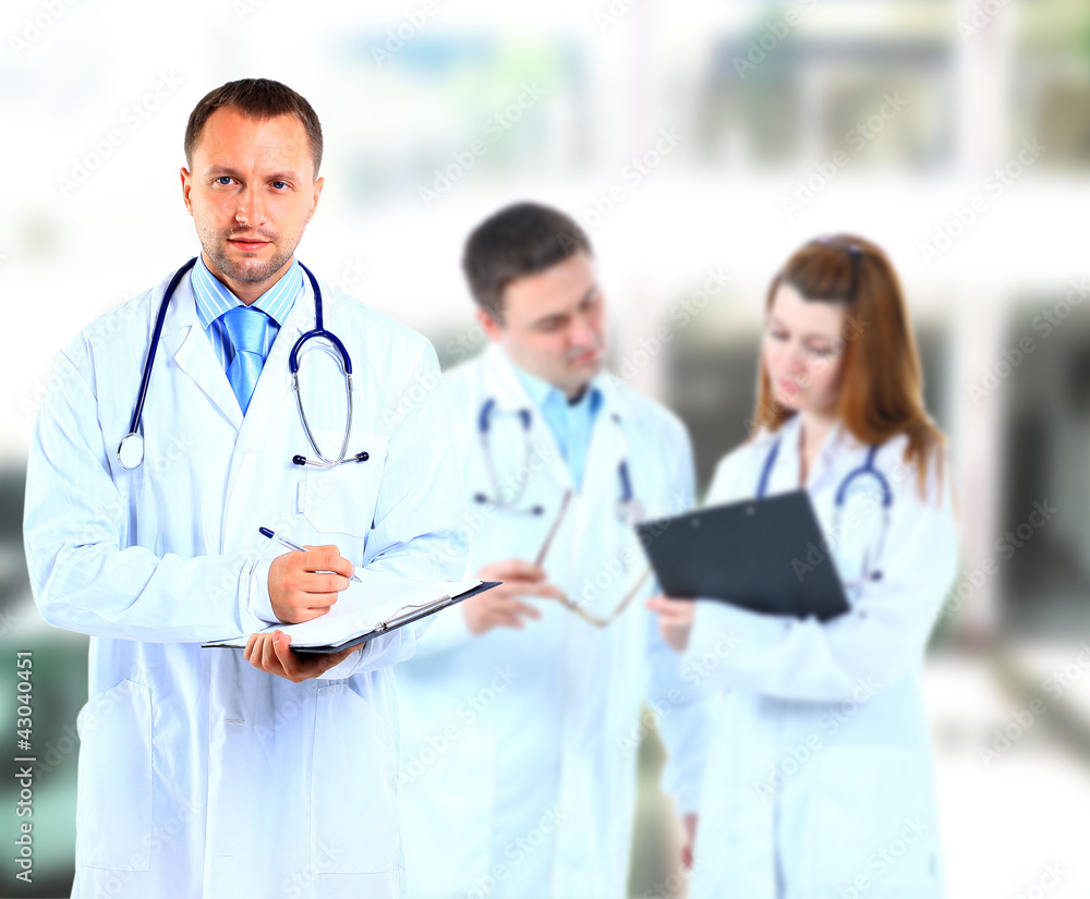 Portrait doctor smiling with colleagues in background Portrait doctor smiling with colleagues in background