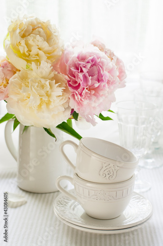 White cups and a bouquet of peonies on the table