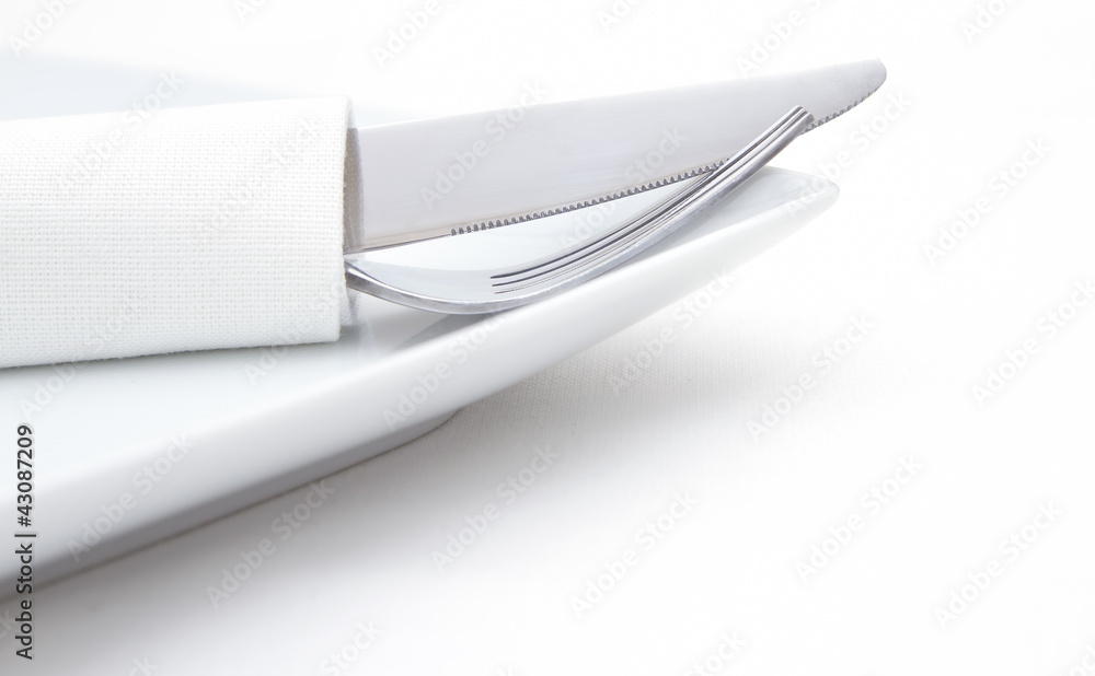 Place setting, silverware in napkin on white plate Place setting, silverware in napkin on white plate