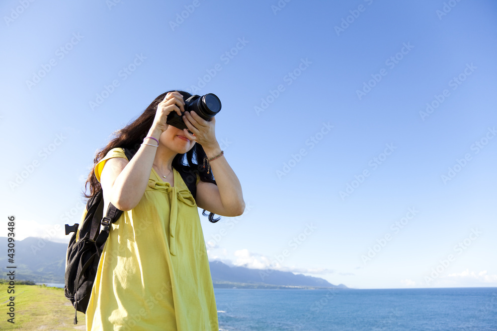 Young woman with backpack standing on the hill taking photo