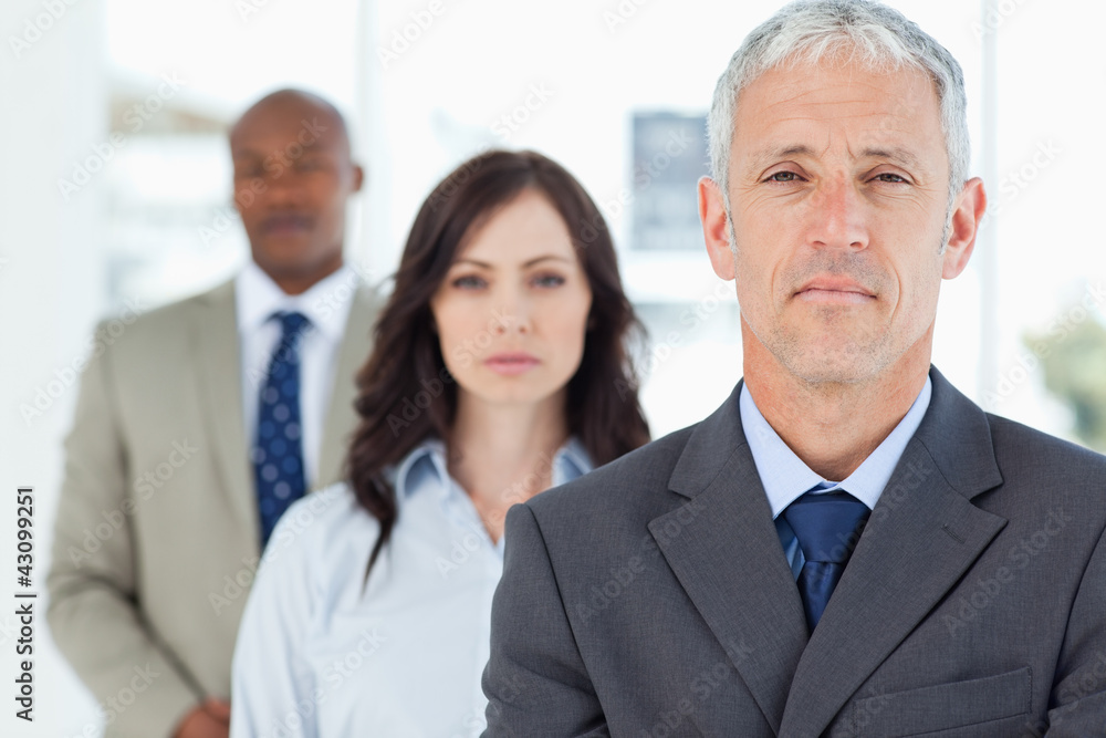 Mature and serious manager standing upright and followed by two Mature and serious manager standing upright and followed by two