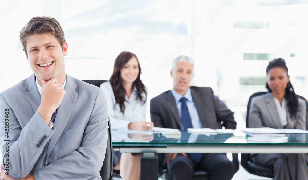 Smiling young executive sitting in front of his team with his ha Smiling young executive sitting in front of his team with his ha