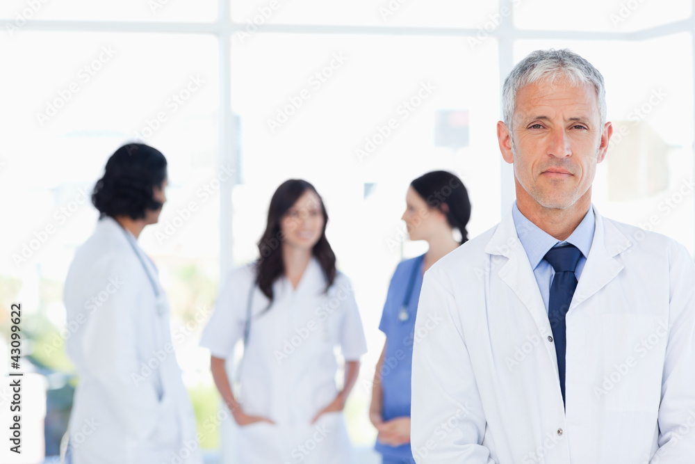 Mature doctor standing in the foreground and accompanied by his