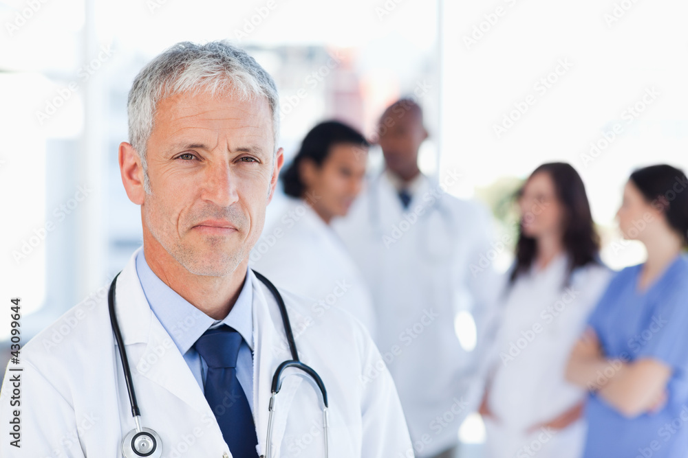 Mature doctor looking straight ahead while his team is looking a Mature doctor looking straight ahead while his team is looking a