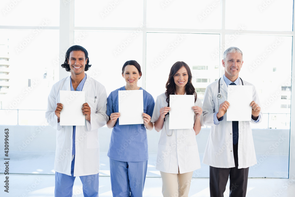 Four medical people standing upright while holding blank sheets Four medical people standing upright while holding blank sheets