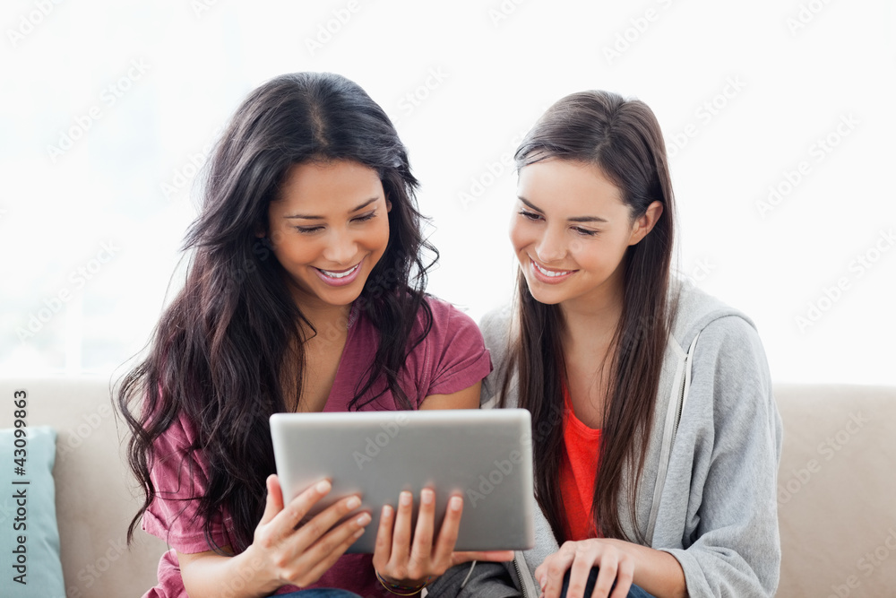 A woman with her friend smiling as they both look at the tablet A woman with her friend smiling as they both look at the tablet