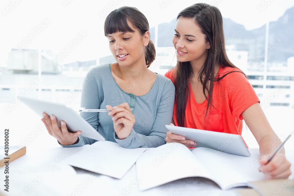 Two smiling students using tablets with one girl looking at the Two smiling students using tablets with one girl looking at the