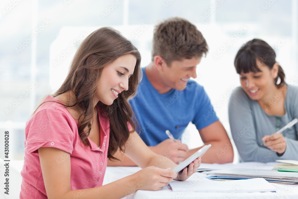 A girl looks at the tablet screen as she smiles with friends A girl looks at the tablet screen as she smiles with friends