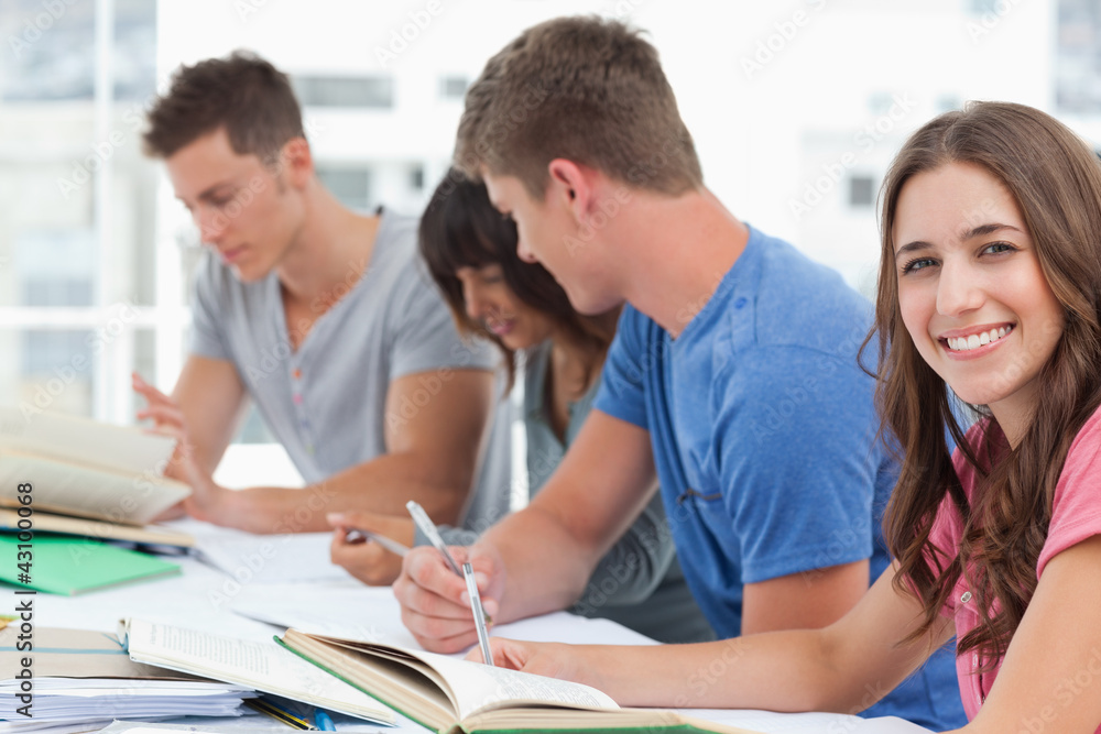 A side view of people studying as one girl looks into the camera A side view of people studying as one girl looks into the camera