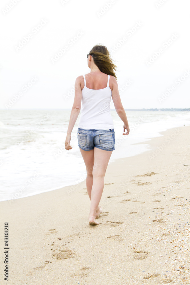 Woman in denim shorts walking on beach Woman in denim shorts walking on beach