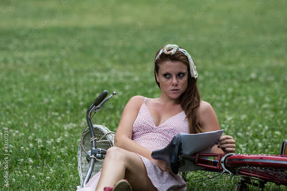 Beautiful girl with her bicycle, in a garden while is reading