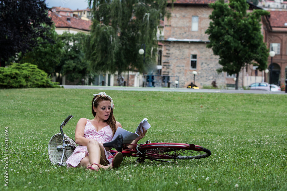 Beautiful girl with her bicycle, in a garden while is reading