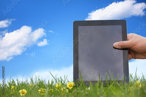 Hand holding tablet pc on meadow