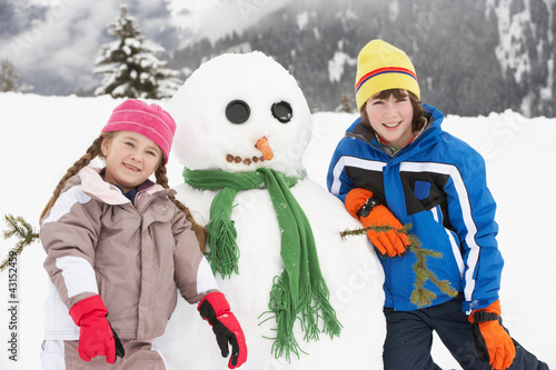 Two Young Children Building Snowman On Ski Holiday In Mountains